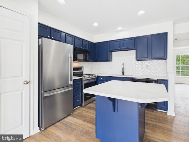 kitchen featuring blue cabinets, a sink, a kitchen bar, wood finished floors, and stainless steel appliances