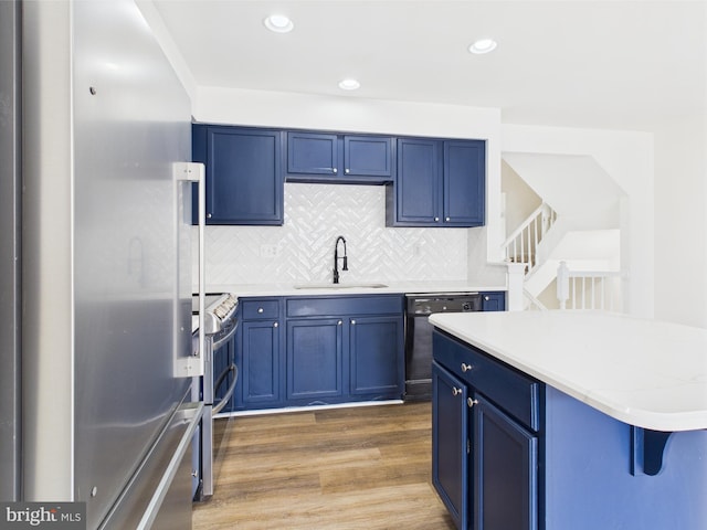 kitchen with a sink, wood finished floors, blue cabinets, backsplash, and appliances with stainless steel finishes
