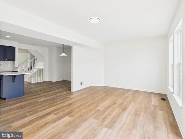 unfurnished living room featuring a wealth of natural light, stairway, baseboards, and light wood-type flooring