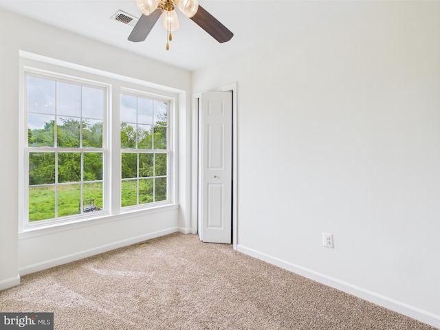 empty room with baseboards, ceiling fan, light carpet, and visible vents