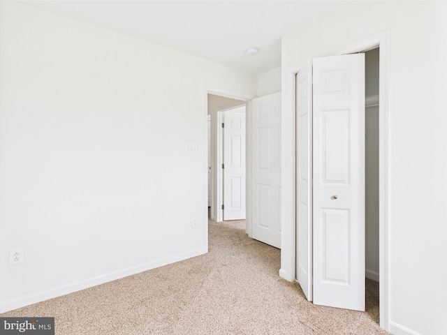 unfurnished bedroom with a closet, light carpet, and baseboards