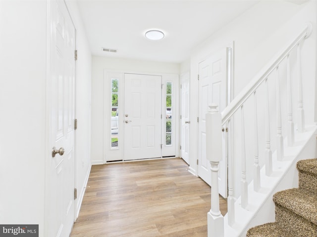 foyer entrance with stairs, light wood finished floors, and visible vents