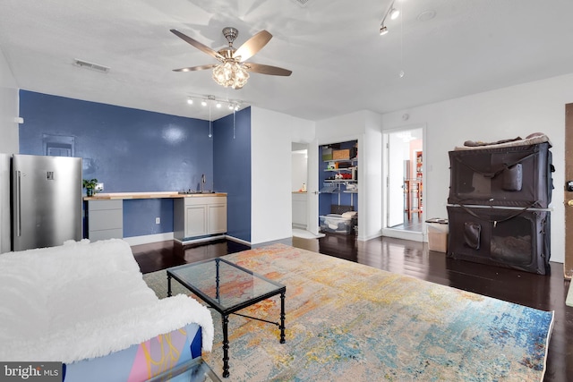 living room featuring ceiling fan, track lighting, visible vents, baseboards, and wood finished floors
