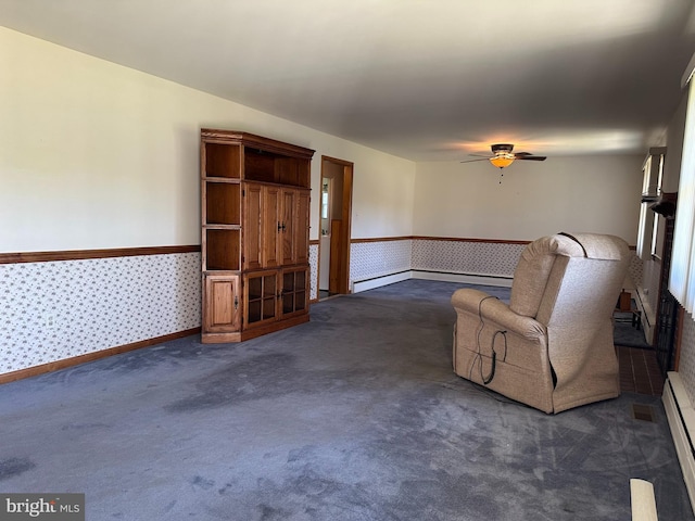 unfurnished living room with dark colored carpet, ceiling fan, wallpapered walls, and wainscoting
