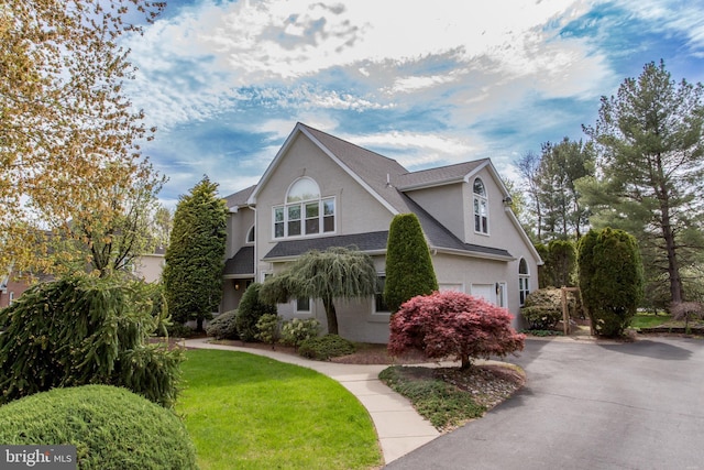 view of front of home with roof with shingles, a front lawn, aphalt driveway, a garage, and stucco siding