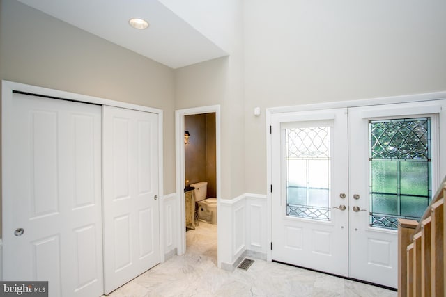 foyer featuring french doors, marble finish floor, a decorative wall, and a wainscoted wall