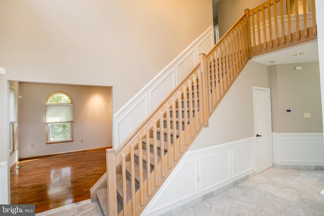 stairs with a decorative wall, wood finished floors, a wainscoted wall, and a towering ceiling