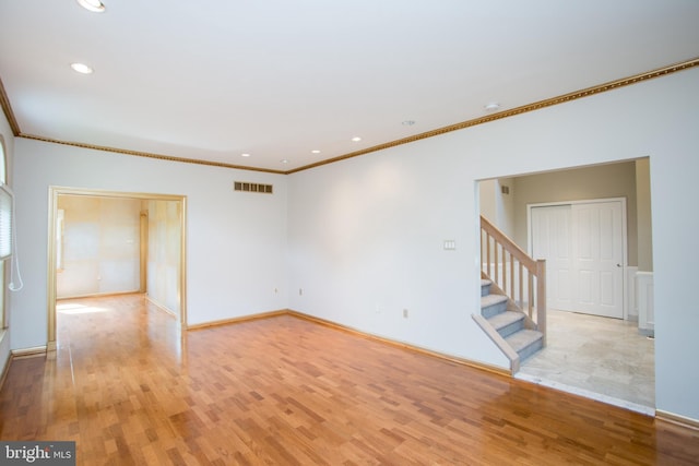 spare room with visible vents, ornamental molding, light wood finished floors, and stairway