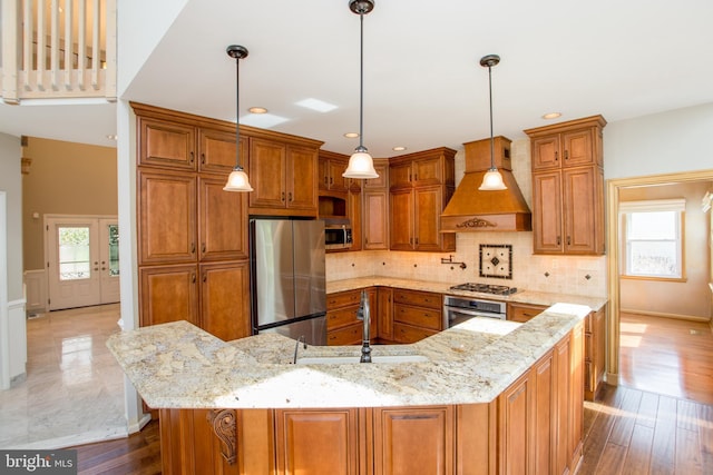 kitchen featuring light stone countertops, premium range hood, brown cabinets, a sink, and appliances with stainless steel finishes