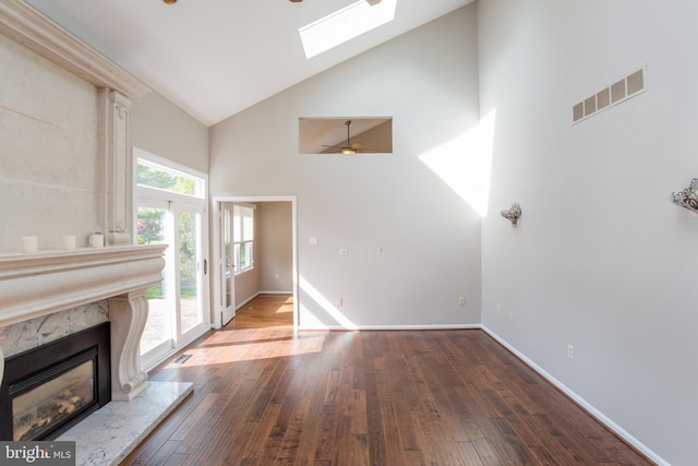 unfurnished living room with ceiling fan, visible vents, a skylight, wood finished floors, and high vaulted ceiling