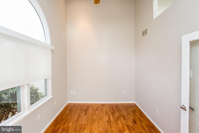 unfurnished room featuring light wood-style floors, baseboards, a high ceiling, and visible vents