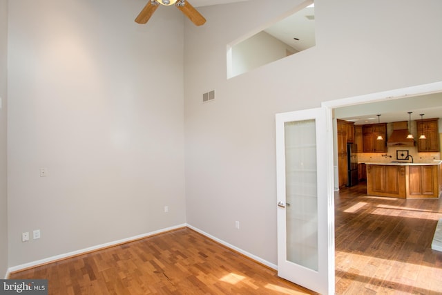 unfurnished room featuring a ceiling fan, a high ceiling, baseboards, and light wood finished floors