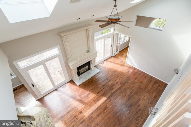 unfurnished living room with a ceiling fan, a skylight, a fireplace, light wood-type flooring, and high vaulted ceiling