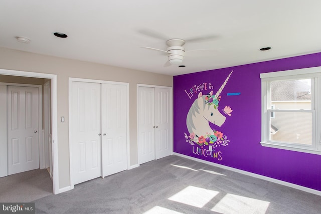 unfurnished bedroom with carpet floors, baseboards, multiple closets, and ceiling fan