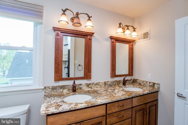 bathroom with double vanity, toilet, visible vents, and a sink
