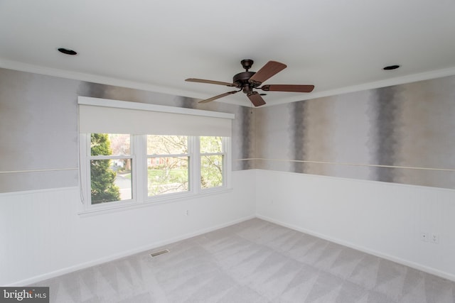 empty room with crown molding, light carpet, a ceiling fan, and visible vents