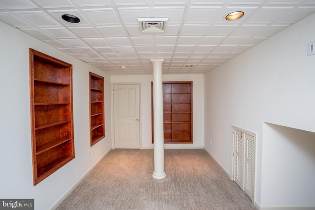 below grade area featuring visible vents, baseboards, built in shelves, and light colored carpet