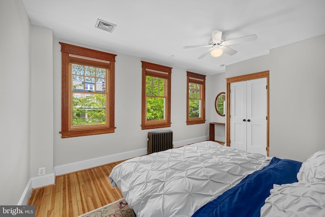 bedroom with radiator, baseboards, wood finished floors, visible vents, and a closet
