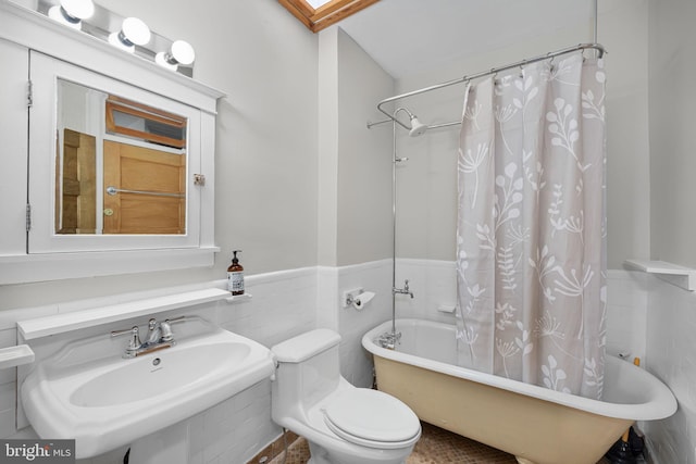full bath featuring a sink, toilet, a wainscoted wall, tile walls, and shower / tub combo