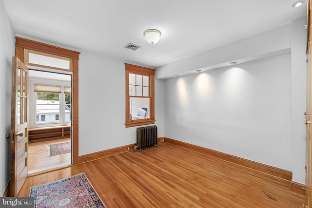 spare room featuring radiator heating unit, baseboards, light wood finished floors, and visible vents