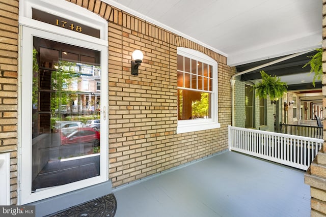doorway to property with a porch and brick siding