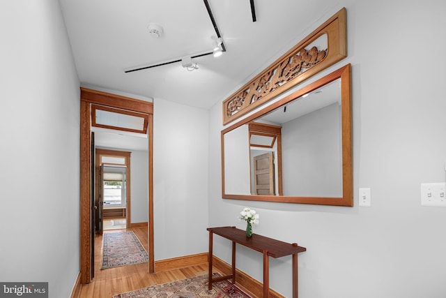 hall with light wood-style floors, baseboards, and track lighting