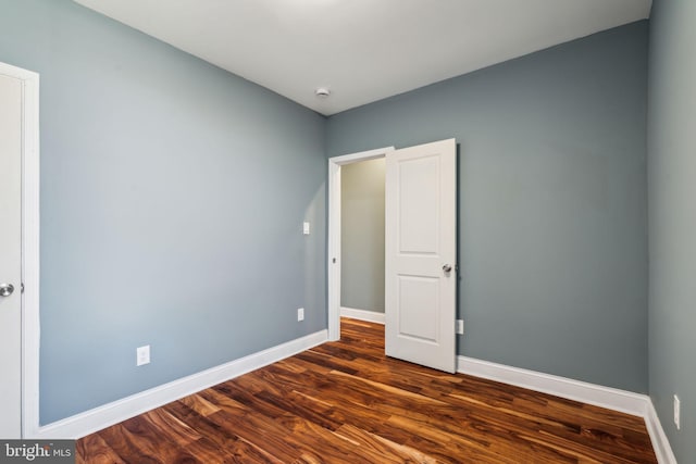 spare room with baseboards and dark wood-style floors