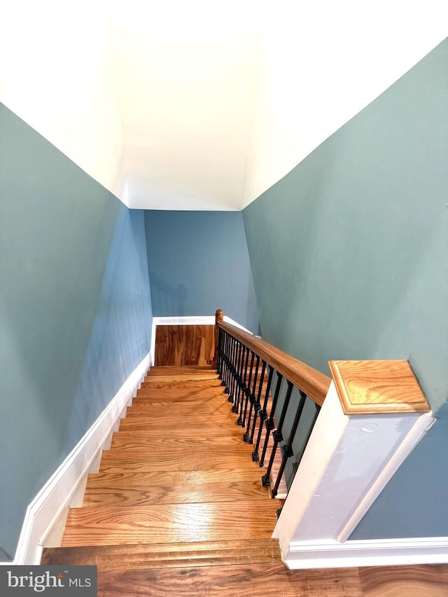 stairs featuring baseboards, wood finished floors, and lofted ceiling