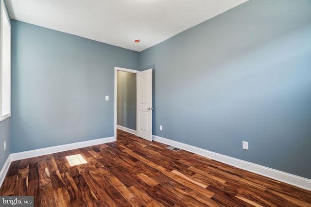 spare room featuring baseboards, visible vents, and dark wood finished floors