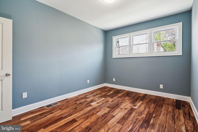 spare room featuring visible vents, dark wood finished floors, and baseboards