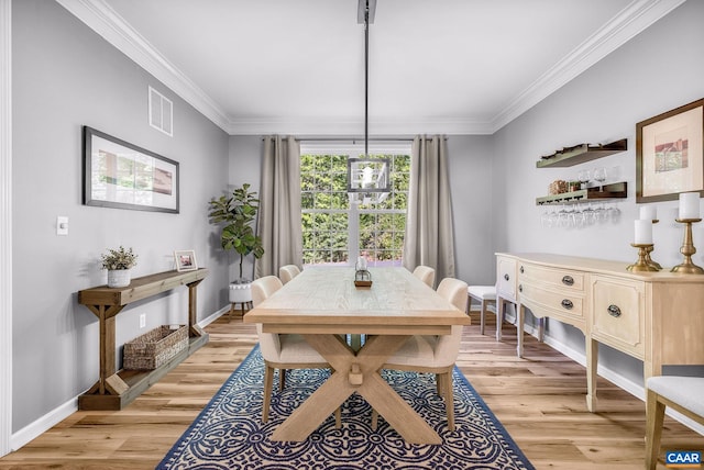 dining area featuring baseboards, visible vents, ornamental molding, and light wood finished floors