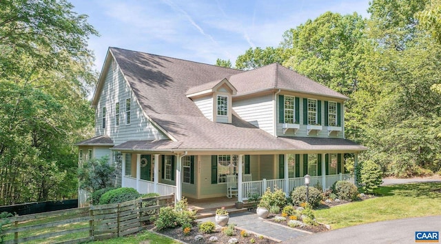 view of front of house featuring a porch, a shingled roof, and fence