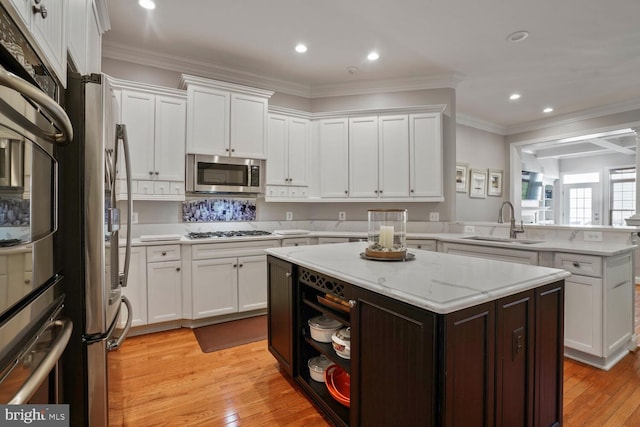 kitchen with stainless steel appliances, a sink, a peninsula, white cabinetry, and ornamental molding