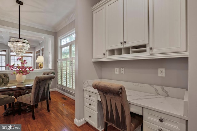 home office featuring built in desk, wood-type flooring, ornamental molding, a chandelier, and baseboards