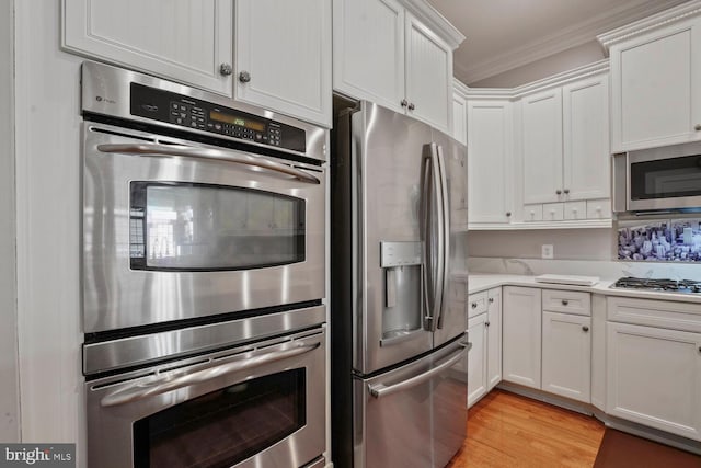 kitchen with appliances with stainless steel finishes, crown molding, white cabinetry, light countertops, and light wood-style floors