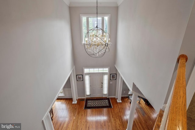 foyer with wood finished floors, a chandelier, baseboards, a towering ceiling, and crown molding