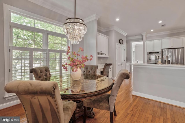 dining room featuring light wood finished floors, a chandelier, baseboards, recessed lighting, and ornamental molding
