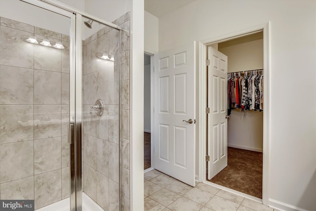 full bathroom featuring a walk in closet, tile patterned flooring, baseboards, and a stall shower