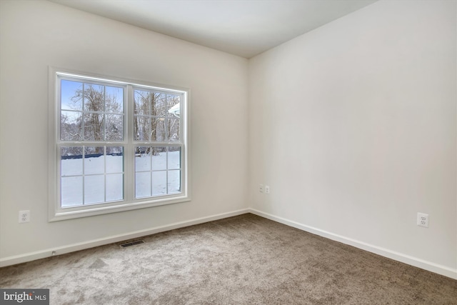 carpeted spare room featuring baseboards, visible vents, and plenty of natural light