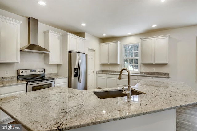 kitchen featuring recessed lighting, wall chimney exhaust hood, white cabinetry, a sink, and appliances with stainless steel finishes