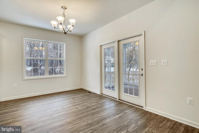 unfurnished dining area featuring plenty of natural light, baseboards, wood finished floors, and a chandelier