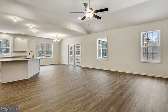 unfurnished living room featuring lofted ceiling, baseboards, dark wood-type flooring, a sink, and ceiling fan with notable chandelier