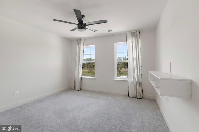empty room with carpet floors, a ceiling fan, baseboards, and visible vents