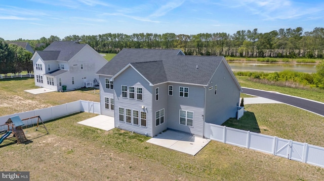 rear view of house with a fenced backyard, a shingled roof, a patio area, a lawn, and a water view