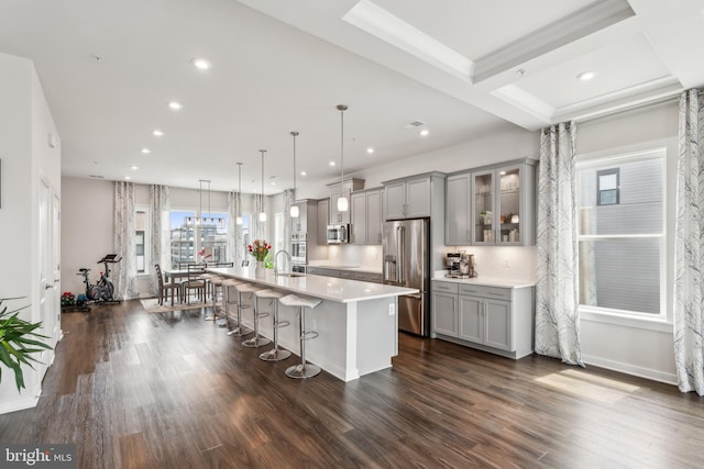 kitchen with a sink, a breakfast bar, stainless steel appliances, a kitchen island with sink, and gray cabinets