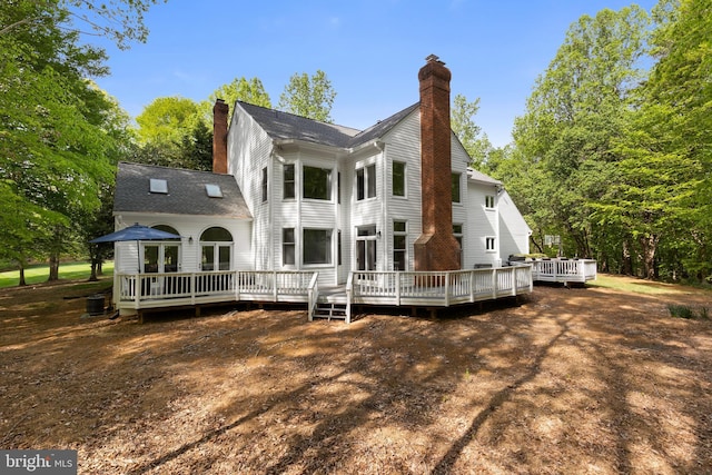 rear view of property featuring cooling unit, a chimney, and a deck