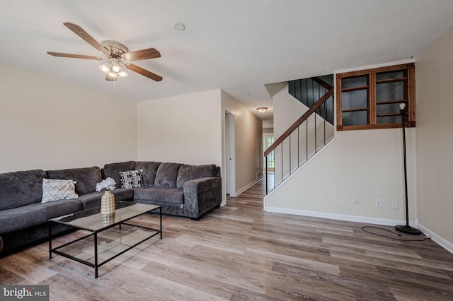 living area featuring baseboards, ceiling fan, stairs, and wood finished floors