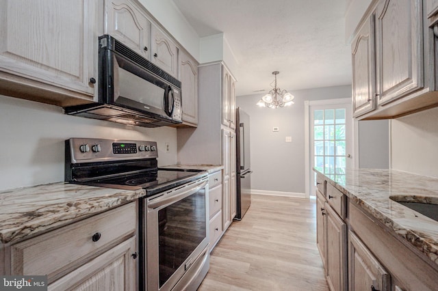 kitchen with black microwave, stainless steel electric range oven, light stone countertops, a notable chandelier, and light wood-style floors