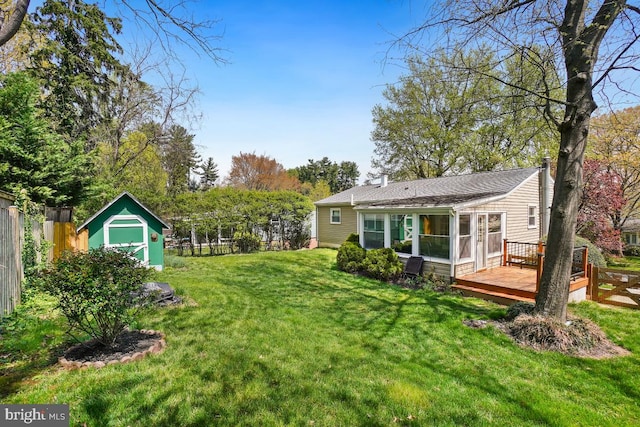 view of yard with a sunroom, an outdoor structure, a deck, a storage unit, and fence