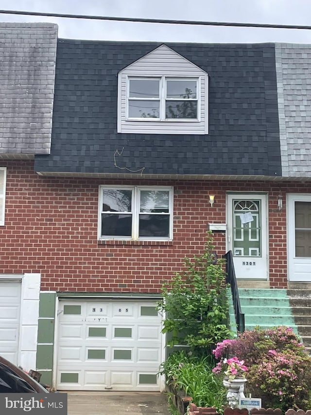 view of front of home with mansard roof, brick siding, a shingled roof, and an attached garage